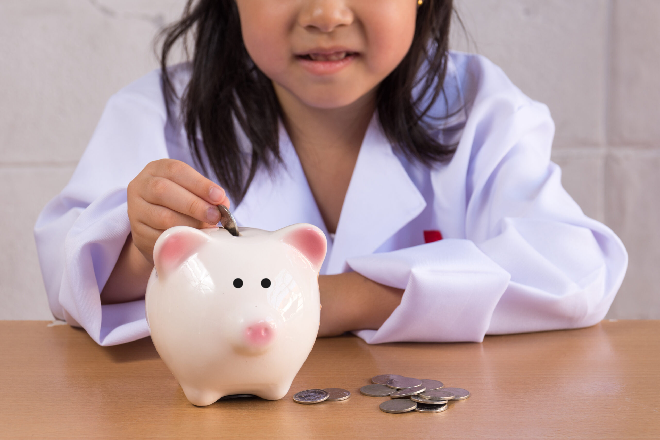 Asian girl playing as a doctor balance money in Piggy Bank